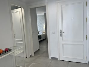 Ein Flur mit einer weißen Tür, einem Bett im Hintergrund und einem Regal mit Orangen.