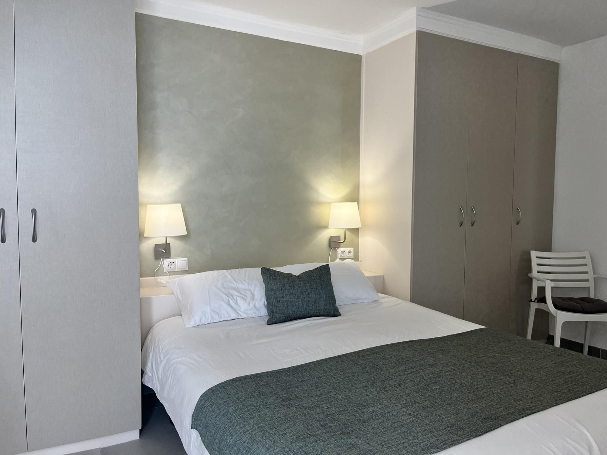 Ein Hotelzimmer mit einem Bett, zwei Nachttischen mit Lampen, einem Sessel und einem Kleiderschrank.