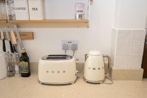 A kitchen counter with a Smeg toaster, a Miele coffee maker, and a shelf above containing labeled containers for coffee, tea, and a can of Grind instant coffee. - Stylish Surbiton Home | 7-Min Walk to Station - Pass the Keys (Surbiton)