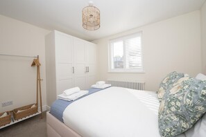 A bedroom with a bed, a wardrobe, a radiator, and a window with blinds. - Stylish Surbiton Home | 7-Min Walk to Station - Pass the Keys (Surbiton)