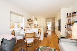 A modern kitchen with white cabinets, a dining area with a table set for four, and a cozy seating area with a sofa and chairs. - Stylish Surbiton Home | 7-Min Walk to Station - Pass the Keys (Surbiton)