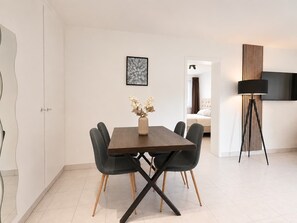 Een moderne eetruimte met een houten tafel en zwarte stoelen, een vaas met gedroogde bloemen en een kunstwerk in een lijst aan de muur.