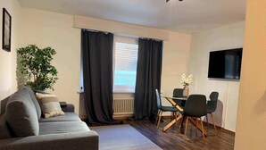 A modern living room with a sofa, a dining table with chairs, a potted plant, and a radiator. - book2stay: Apartment 2.5-room Biel (Biel)