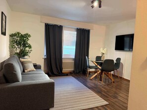 Ein modernes Wohnzimmer mit einer Couch, einem Esstisch mit Stühlen, einer Topfpflanze und einer Heizung.