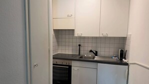 A compact kitchen with white cabinets, a black countertop, a sink, and an oven. - book2stay: Apartment 2.5-room Biel (Biel)