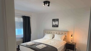 A neatly made bed with a checkered throw, a bedside lamp, and a cityscape artwork on the wall. - book2stay: Apartment 2.5-room Biel (Biel)