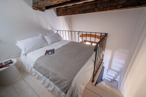 A bedroom with a bed, a bedside table with books, a wooden ceiling beam, and a window. - Casa Magnoli by MMega (Firenze)