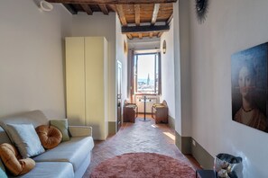 A cozy living room with a sofa, a coffee table, and a view of a cityscape through an open door. - Casa Magnoli by MMega (Firenze)