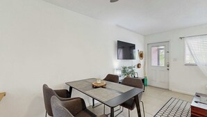 Un comedor con una mesa y sillas, un televisor de pantalla plana montado en la pared y una puerta con ventanal.