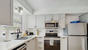 Una cocina moderna con armarios blancos, microondas integrado, estufa y refrigerador.