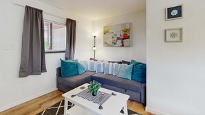 Una sala de estar moderna con un sofá seccional gris, una mesa de centro blanca con una planta, y una lámpara de pie.
