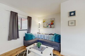 Ein modernes Wohnzimmer mit einem grauen Ecksofa, einem weißen Couchtisch mit Pflanze und einer Stehlampe.