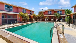 Una piscina con agua cristalina y azul, rodeada por una valla y contigua a un edificio de fachada roja.