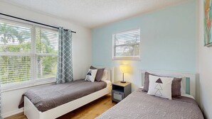 Un dormitorio con dos camas individuales, una mesita de noche con lámpara y una ventana con persianas.
