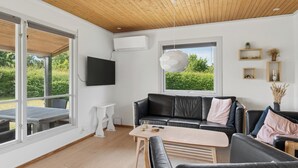 Una sala de estar moderna con un sofá de cuero negro, una mesa de centro de madera y un televisor montado en la pared.