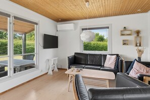 A modern living room with a black leather sofa, a wooden coffee table, and a television mounted on the wall. - Holiday Near Beach and Coastal Nature (Gørlev)