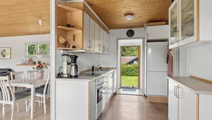 Una cocina moderna con armarios blancos, techo de madera y un comedor con sillas blancas.