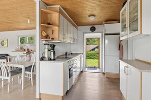 A modern kitchen with white cabinetry, a wooden ceiling, and a dining area with white chairs. - Holiday Near Beach and Coastal Nature (Gørlev)