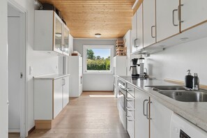 Una cocina moderna con armarios blancos, techo de madera y ventana con vistas a la vegetación.