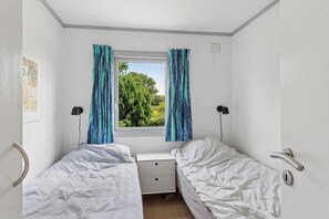 Habitació petita i ben il·luminada amb dos llits individuals, una tauleta de nit i una finestra amb cortines.