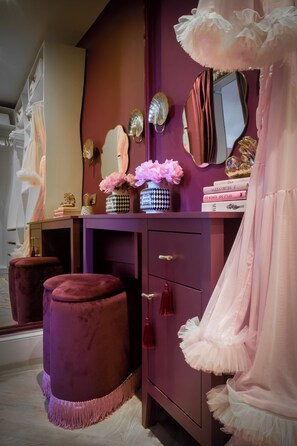 Un comò con specchio, un tavolo da trucco e un abito rosa su una parete viola.