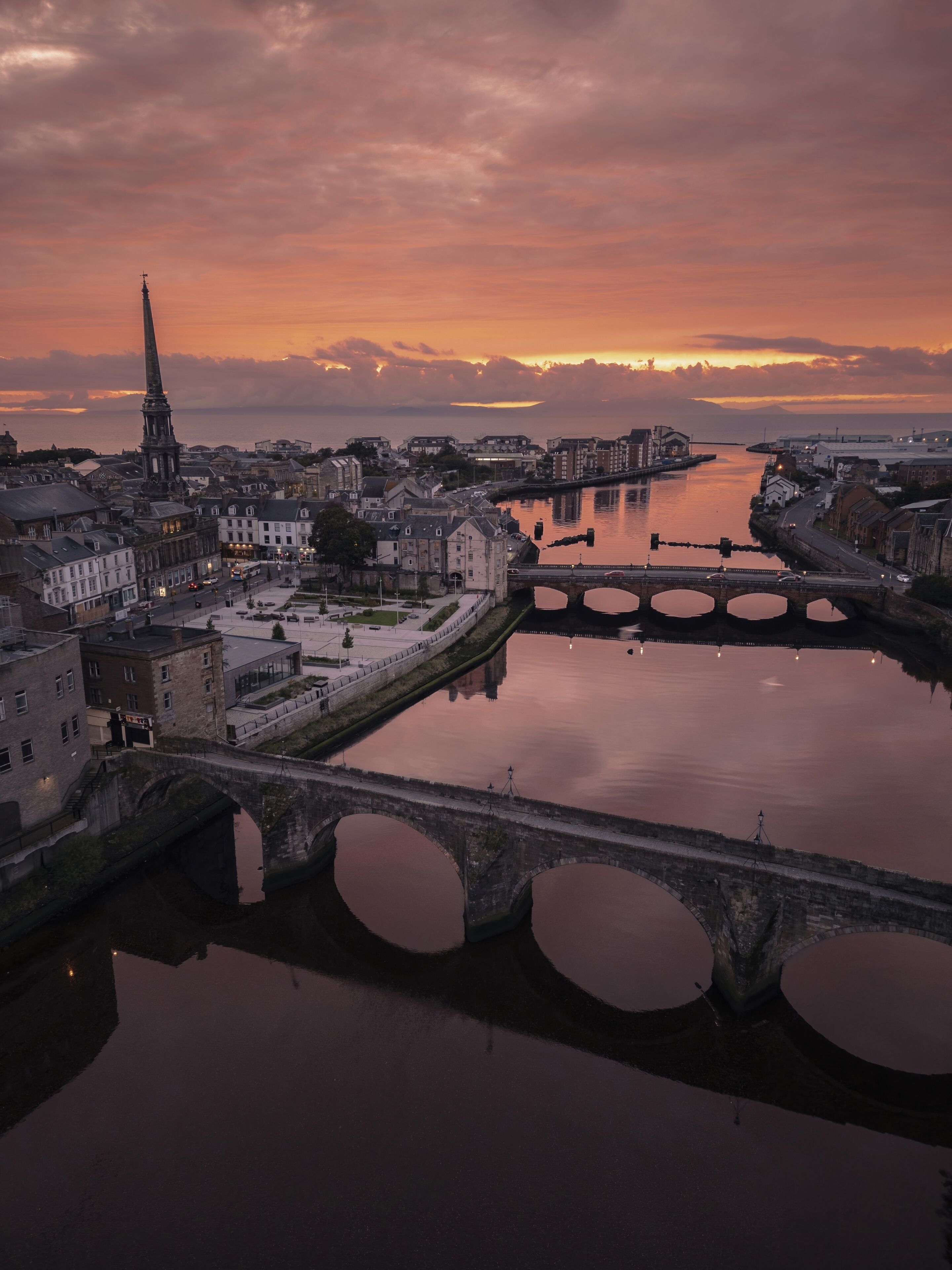 A cityscape with a prominent tower, a river with bridges, and a sunset.