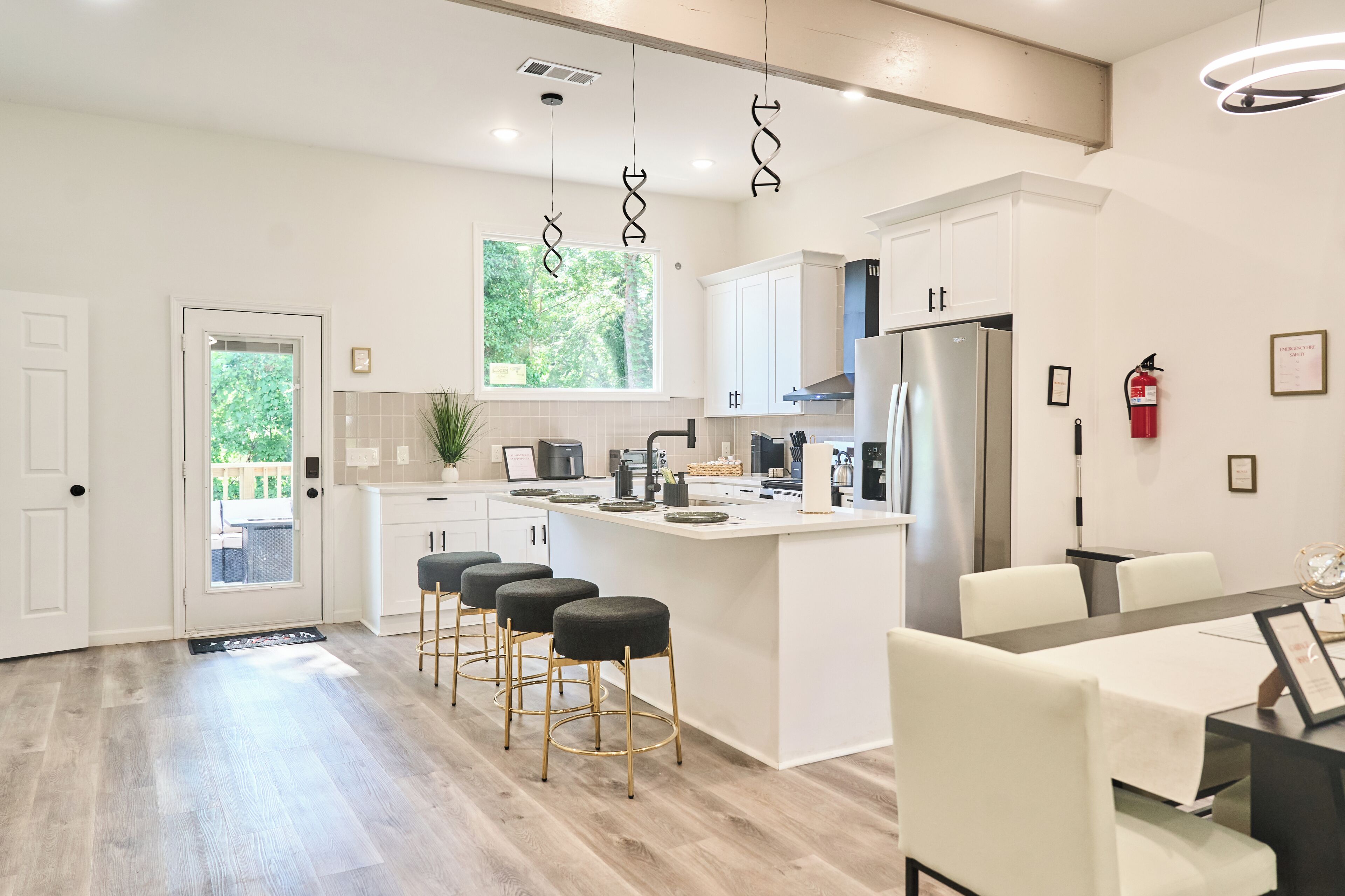 Una cocina moderna con gabinetes blancos, un refrigerador de acero inoxidable y una barra con taburetes.