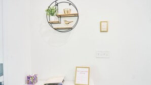 En hvid væg med en rund metalkasse, der indeholder en plante, en fuglefigur og en krone. Under den, et hvidt bord med en lilla æske, et indrammet certifikat og et magasin.