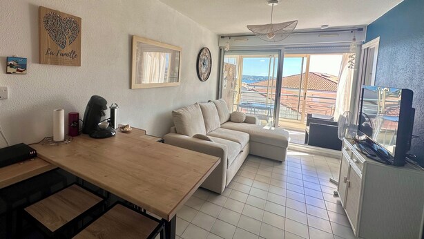 En stue med sofa, spisebord, fjernsyn og en balkon med udsigt.