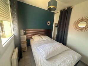 Ein Schlafzimmer mit einem Bett, einem Nachttisch, einer Lampe, einem Fenster mit Jalousien und einem Wanddekor.