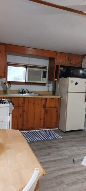 Een kleine keuken met houten kastjes, een witte koelkast en een magnetron.