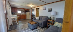 A compact living space with a kitchenette, a sofa, a small table, and a lamp. - West Battle Seasonal Cabin (Henning)