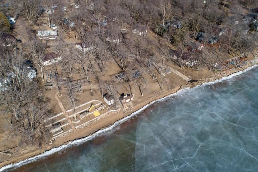 An aerial view of a coastal area with houses, trees, and a frozen shoreline.