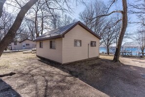 A small, single-story building with a sloped roof, surrounded by trees and a body of water. - West Battle Seasonal Cabin (Henning)