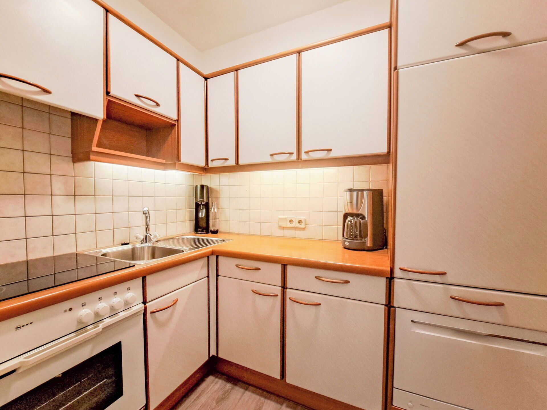 Una cocina con armarios blancos, estufa, lavabo y cafetera.