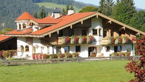 Ein traditionelles Chalet mit rotem Ziegeldach, mehreren Balkonen mit Blumenkästen und Blick auf eine Berglandschaft.