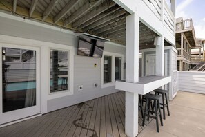 A covered outdoor deck with a bar area, built-in seating, and a TV mounted on the wall. - Steps to Sand-Full Remodel Like New! (Corolla)