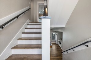 A staircase with wooden steps and white walls, leading to a kitchen area with wooden flooring and a ceiling fan. - Steps to Sand-Full Remodel Like New! (Corolla)