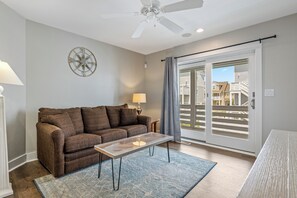 A living room with a brown sofa, a glass coffee table, a lamp, a ceiling fan, and a view through a sliding glass door. - Steps to Sand-Full Remodel Like New! (Corolla)