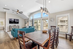A spacious living area with a wooden dining table, blue sofa, and a large window with a view. - Steps to Sand-Full Remodel Like New! (Corolla)