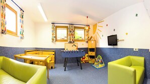 Ein Kinderspielzimmer mit einem Fußballtisch, zwei grünen Sofas und einer Spielecke mit Spielzeug.
