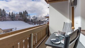 Een balkon met een tafel gedekt voor twee, met uitzicht op een besneeuwd landschap met bomen en een gebouw in de verte.