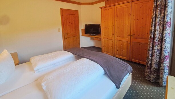 Habitació d'hotel amb llit, armari de fusta, televisió i cortines amb motius florals.
