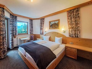 Een hotelkamer met een groot bed, een nachtkastje, gordijnen voor het raam, een radiator en een schilderij aan de muur.