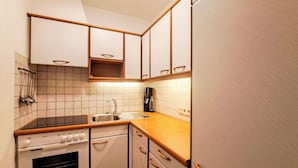 Een compacte keuken met witte kastjes, een roestvrijstalen spoelbak en een ingebouwde oven.