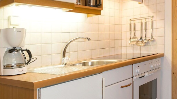 Una cocina compacta con lavamanos, estufa y cafetera.