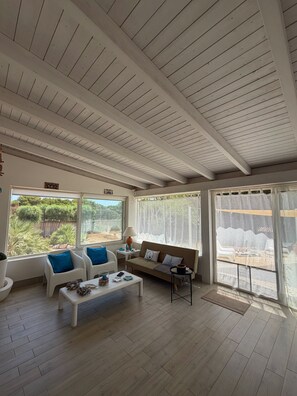 A spacious living area with a high ceiling, a sofa, two armchairs, a coffee table, and a view of the outdoors through large windows. - Villa Faro Sea (San vito lo capo)