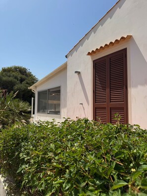 A white building with a large window and brown shutters, surrounded by greenery. - Villa Faro Sea (San vito lo capo)