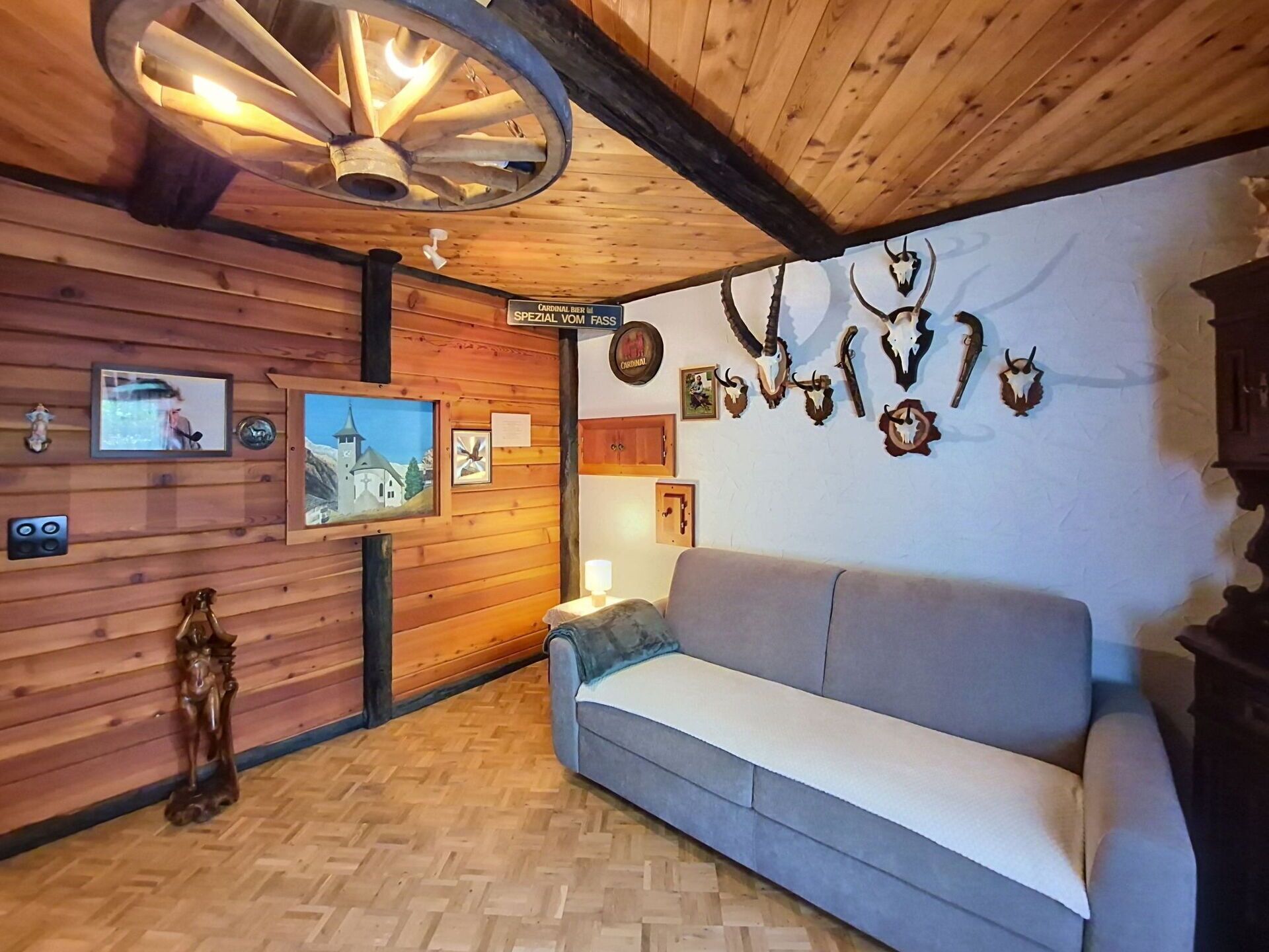 A room with wooden walls, a wooden ceiling, a sofa, a ceiling fan, and wall-mounted decorations including animal skulls.