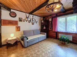 Ein gemütliches Zimmer mit Holzbalkendecke, einem Sofa, einer Lampe, einer Uhr und einem Fenster mit Vorhängen.
